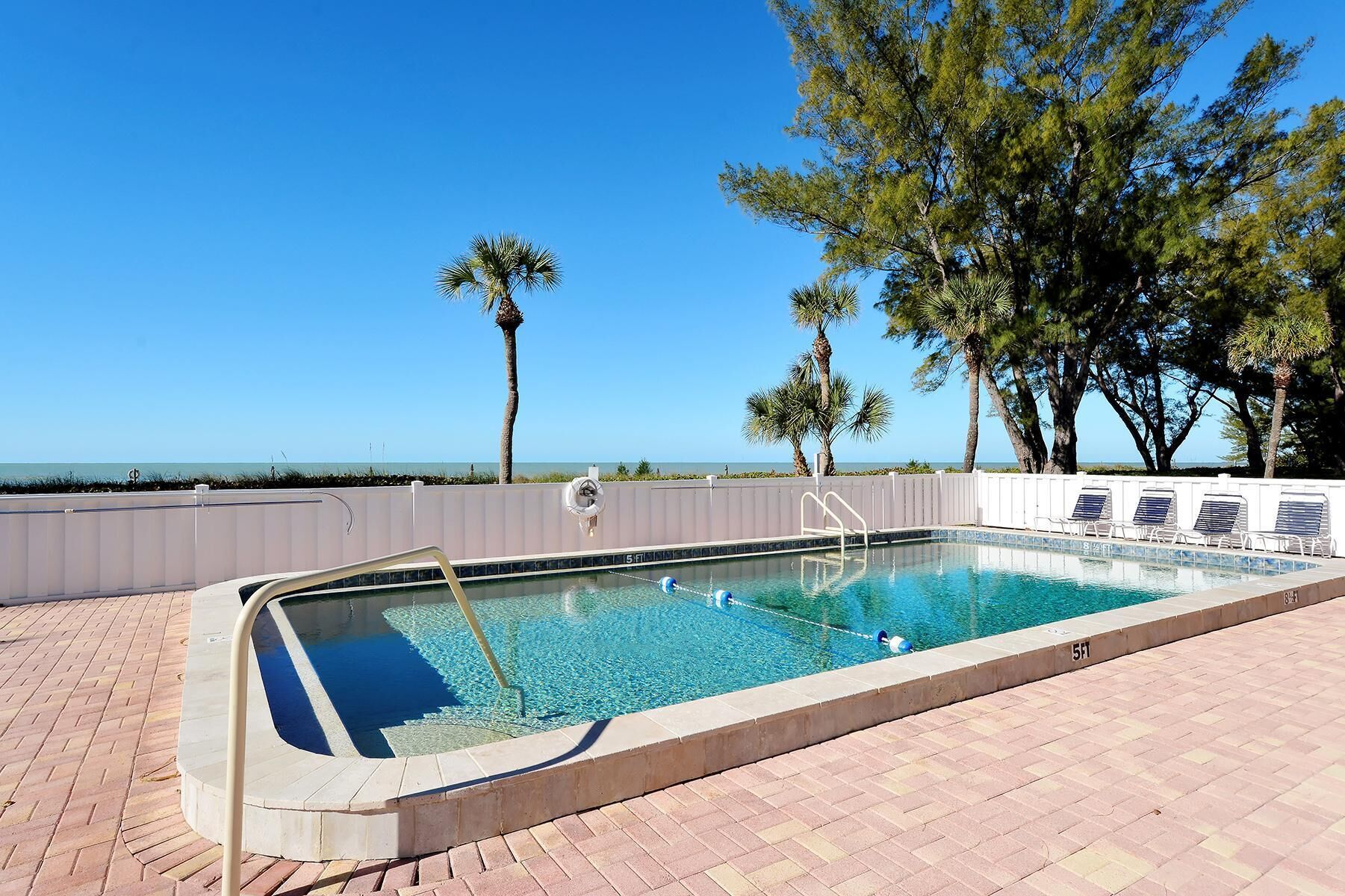 A rectangular swimming pool with a clear blue water, surrounded by a white poolside area with lounge chairs.