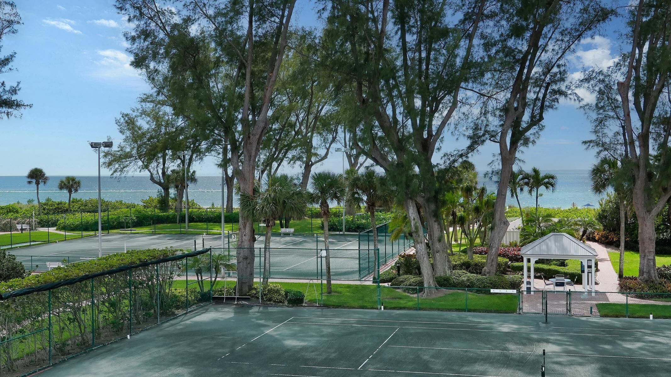 Un court de tennis offrant une vue sur l’océan, entouré d’arbres et agrémenté d’un belvédère.