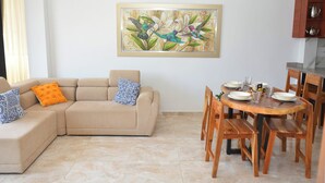Un salon avec un canapé beige, une table à manger avec des chaises et un tableau accroché au mur.