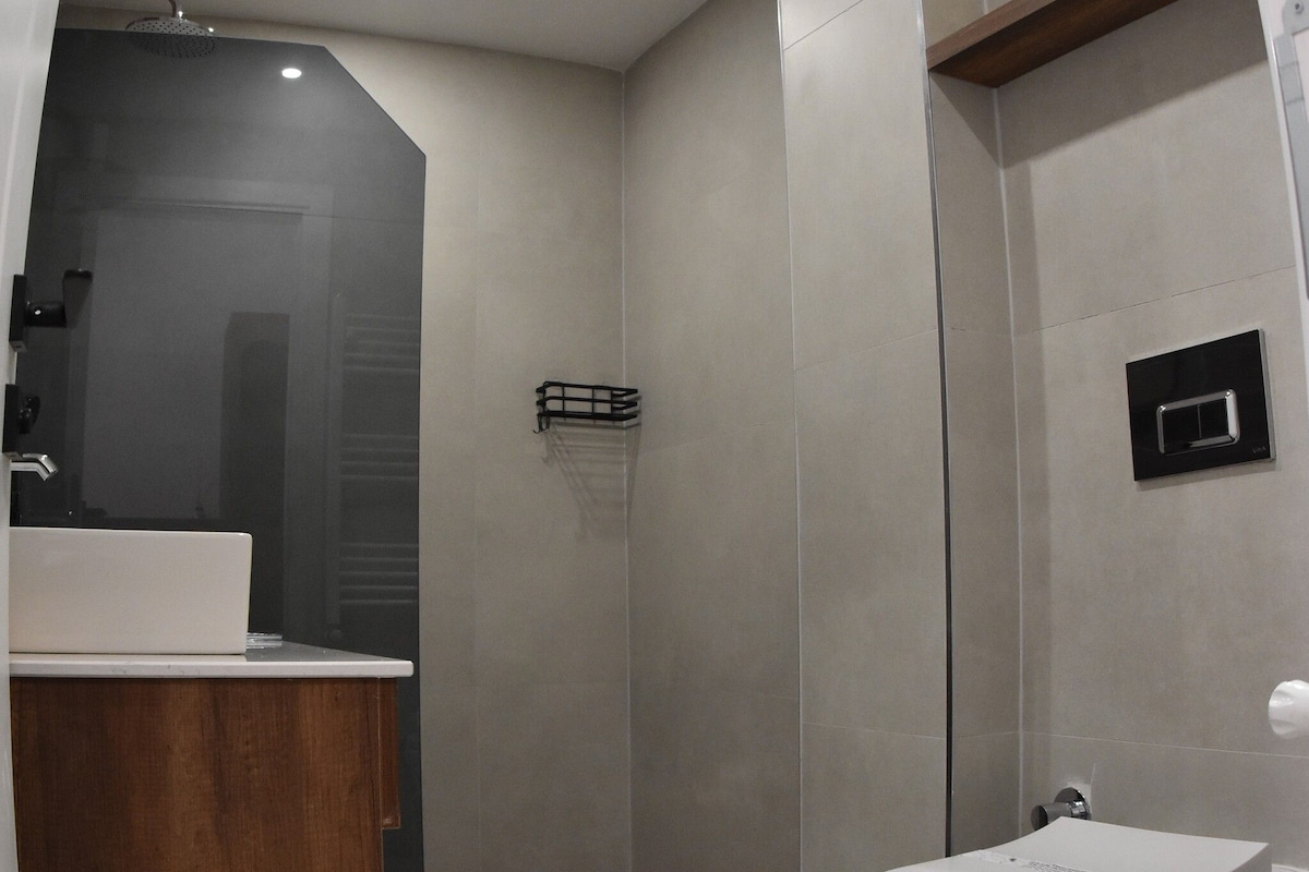 Un baño moderno con tocador de madera, inodoro blanco y zona de ducha.