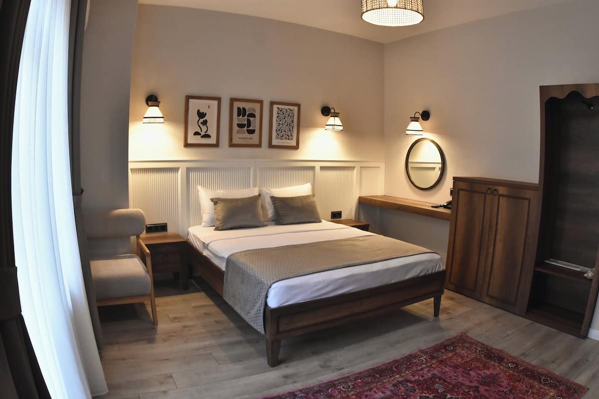 A bedroom with a bed, bedside tables, a chair, a radiator, a mirror, and a door.