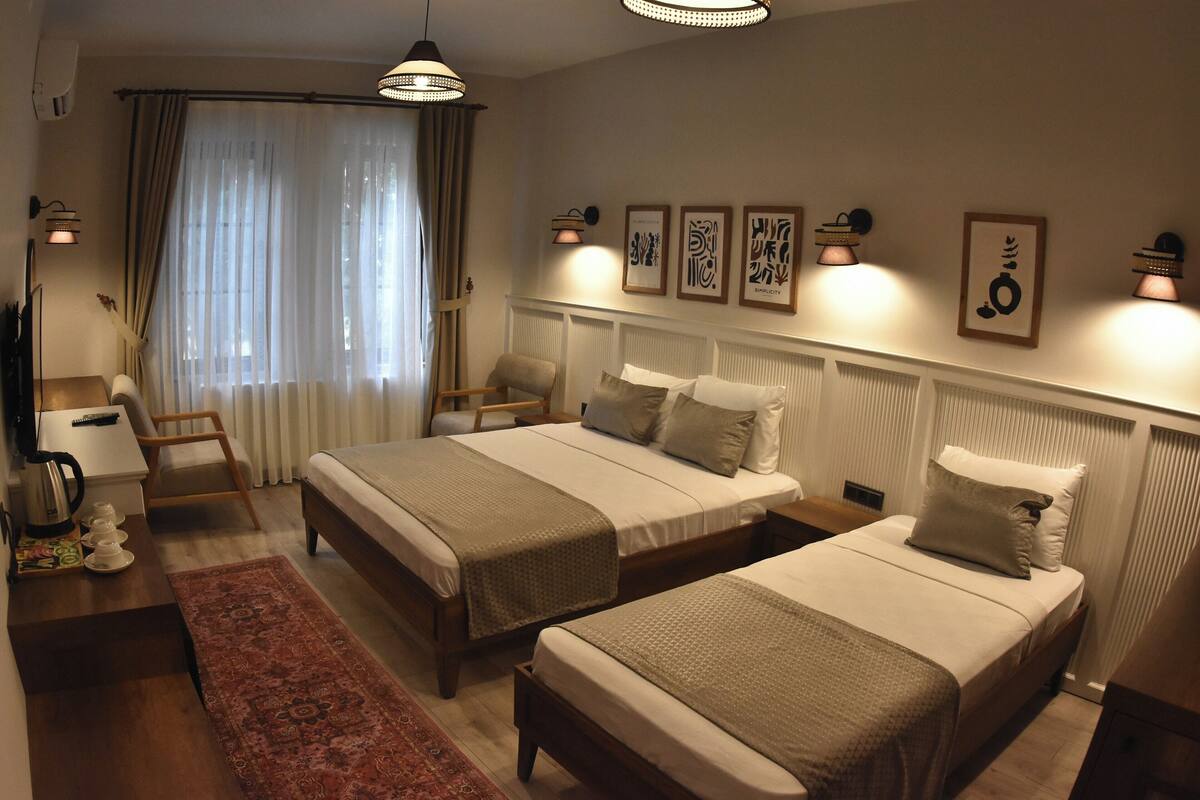 A hotel room with two beds, a desk, a chair, a radiator, and wall-mounted lights.
