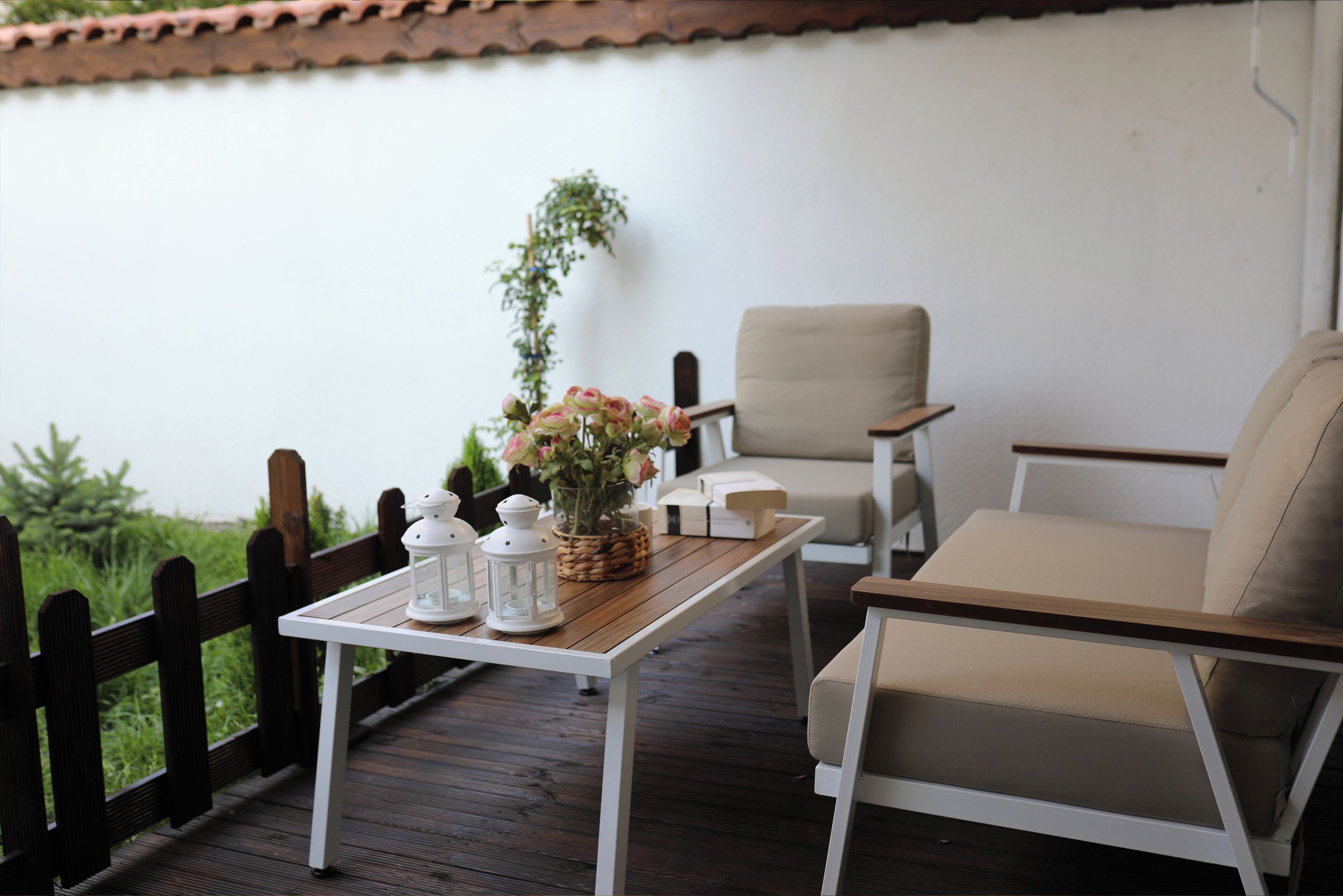 Una terraza de madera con una mesa blanca, dos sillas color beige y una planta en maceta.