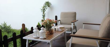 Una terraza de madera con una mesa blanca, dos sillas color beige y una planta en maceta.