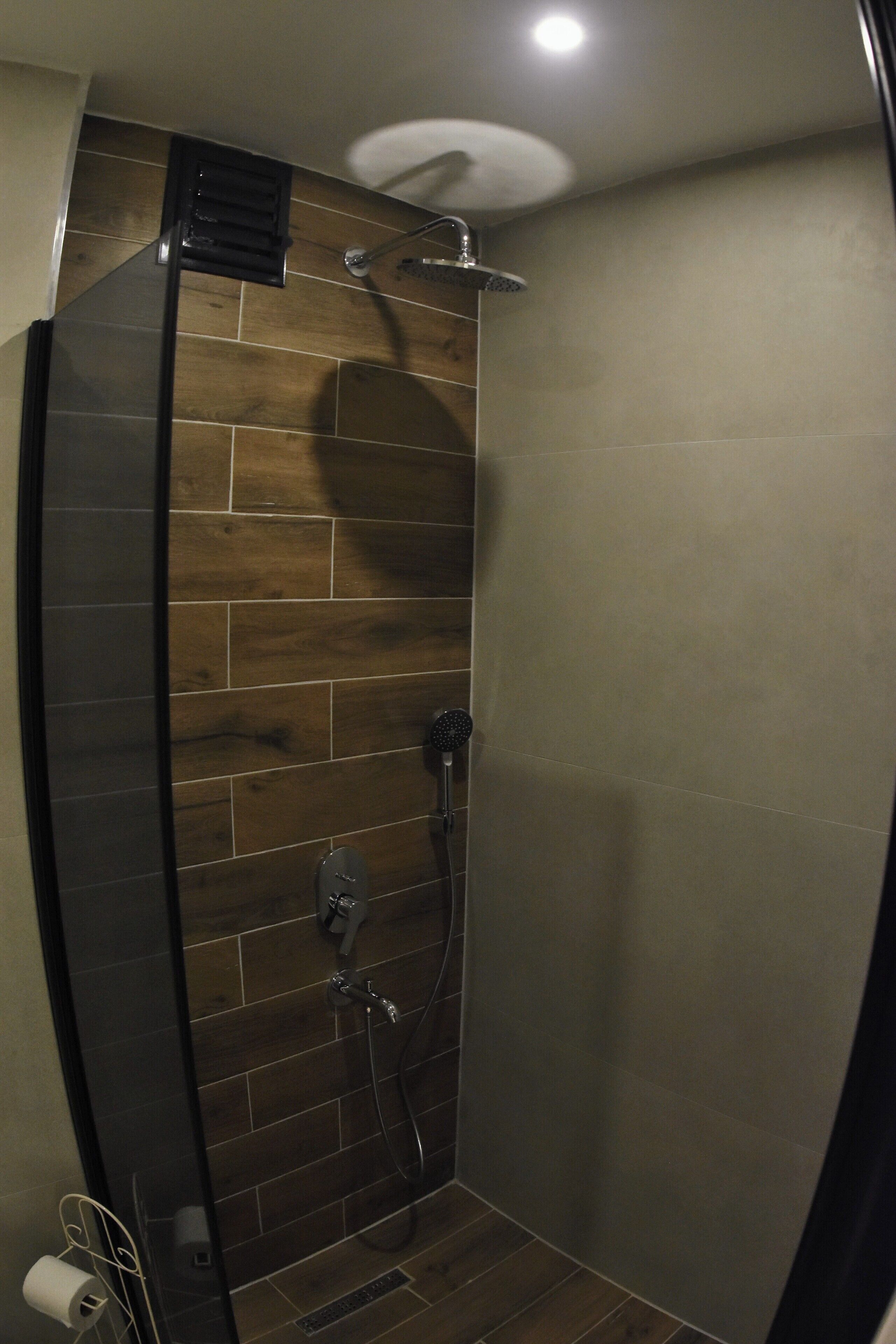 A shower with a wooden panel wall, a glass door, and a ceiling light.