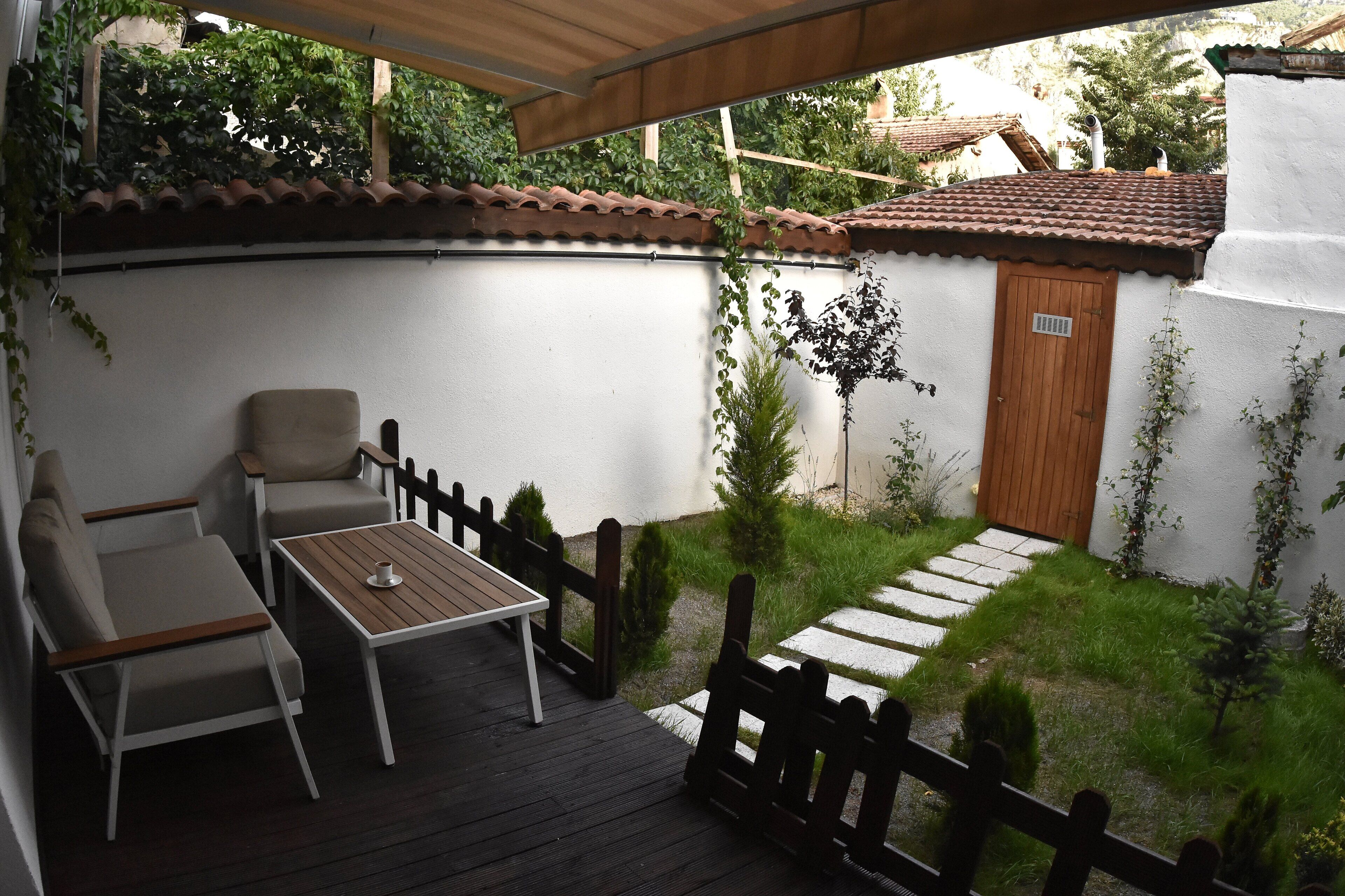 A patio with a wooden table and chairs, a small garden with stepping stones, and a white wall with a wooden door.
