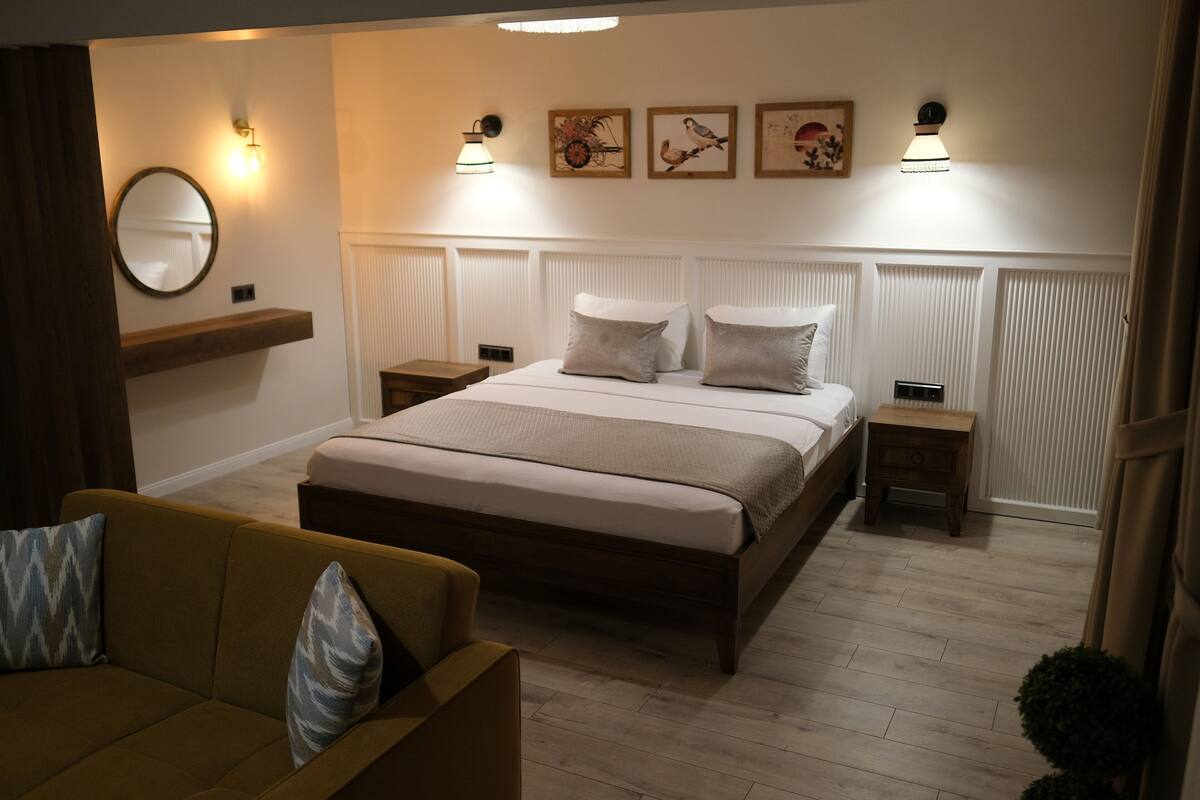 A modern bedroom with a large bed, bedside tables, a sofa, and wall-mounted artwork.
