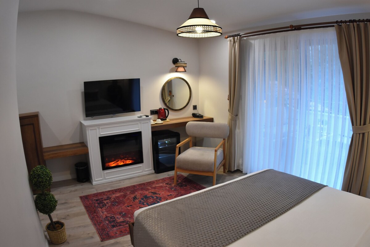 Habitación de hotel con cama, televisión, chimenea, escritorio con silla, espejo y ventana con cortinas.
