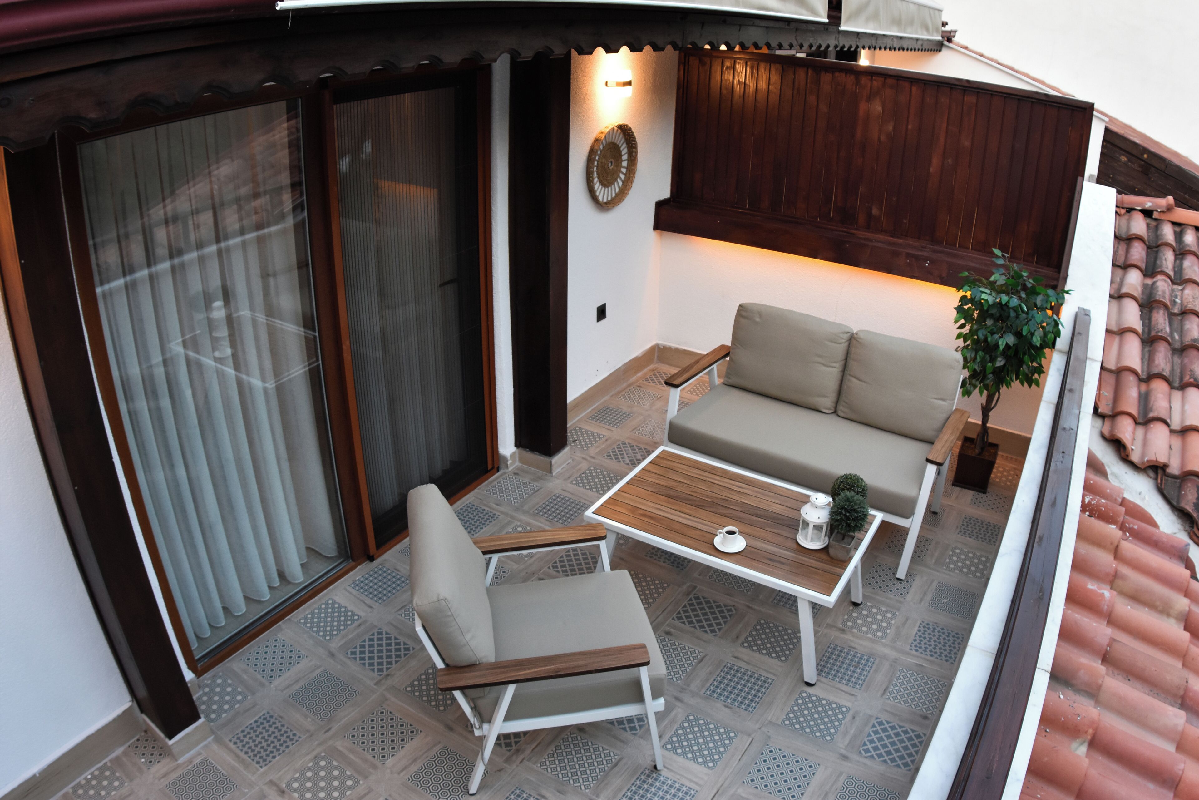 Een balkon met een bank, stoel en tafel, met een betegelde vloer en houten details.