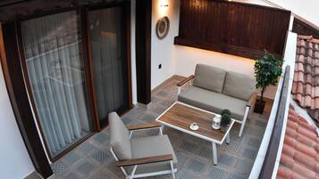 Een balkon met een bank, stoel en tafel, met een betegelde vloer en houten details.