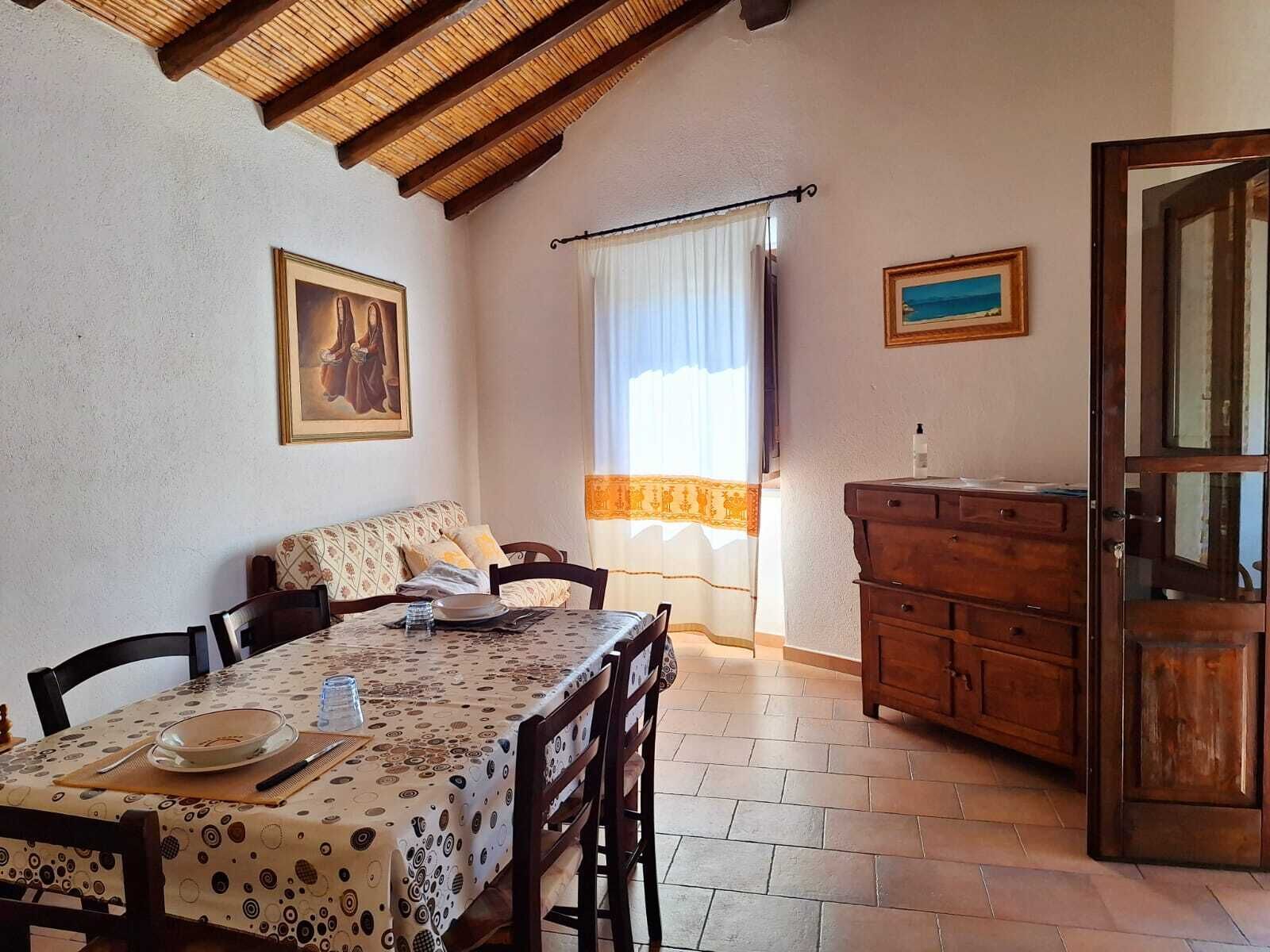 A dining area with a table set for two, a sofa, a wooden cabinet, and a painting on the wall.