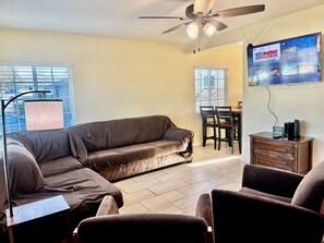 A living room with a sectional sofa, a flat-screen TV mounted on the wall, a ceiling fan, and a dining area with a table and chairs. - Cozy House in East LA (Los Angeles)
