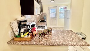 Une cuisine équipée d’un plan de travail en granit, d’une cuisinière, d’un évier et d’un réfrigérateur. On y trouve divers objets sur le plan de travail, notamment une boîte de thé vert, une bouteille de Nescafé et plusieurs pots.