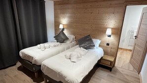 A hotel room with two single beds, wooden headboard, bedside lamps, and a wooden floor. - JARDIN ALPIN 1 - LA PLAGNE TARENTAISE (LA PLAGNE TARENTAISE)