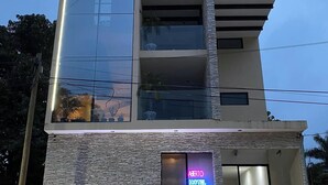 A modern hotel with a stone facade, a glass elevator shaft, and a neon sign for the 'Abertos Hotel'.