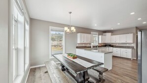 Een ruime keuken met een centraal eiland, witte kasten en een houten eettafel.