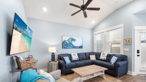 A living room with a sectional sofa, a coffee table, a TV mounted on the wall, and a ceiling fan.