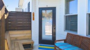 A wooden bench, a small table, and a sofa in a covered outdoor area with a door and windows.