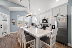 A modern kitchen with white cabinetry, a stainless steel refrigerator, and a central island with bar stools.