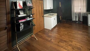 Une pièce avec un plancher en bois, une armoire blanche, une étagère noire et un luminaire au plafond.
