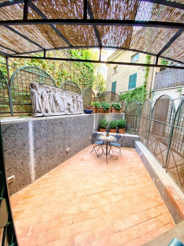 A covered patio area with a stone floor, a table with chairs, and a decorative stone sculpture. - Just a stone's throw from the Spanish Steps, a beautiful apartment surrounded by greenery (Roma)