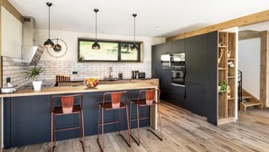 A modern kitchen with a central island, bar stools, a large window, and a staircase leading to an upper level. - CHALET DES EPICURIENS (AIME LA PLAGNE)