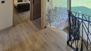 A modern interior with wooden beams, a bed, a glass wall, and a balcony with a railing. - CHALET DES EPICURIENS (AIME LA PLAGNE)