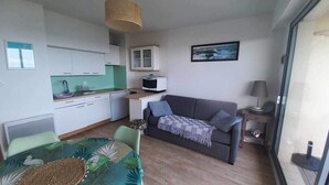 Un espacio habitable compacto con kitchenette, zona de comedor, sofá y una pequeña mesa.