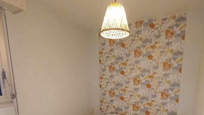Un dormitorio con una cama individual, una lámpara colgante y un papel tapiz estampado con motivos florales.