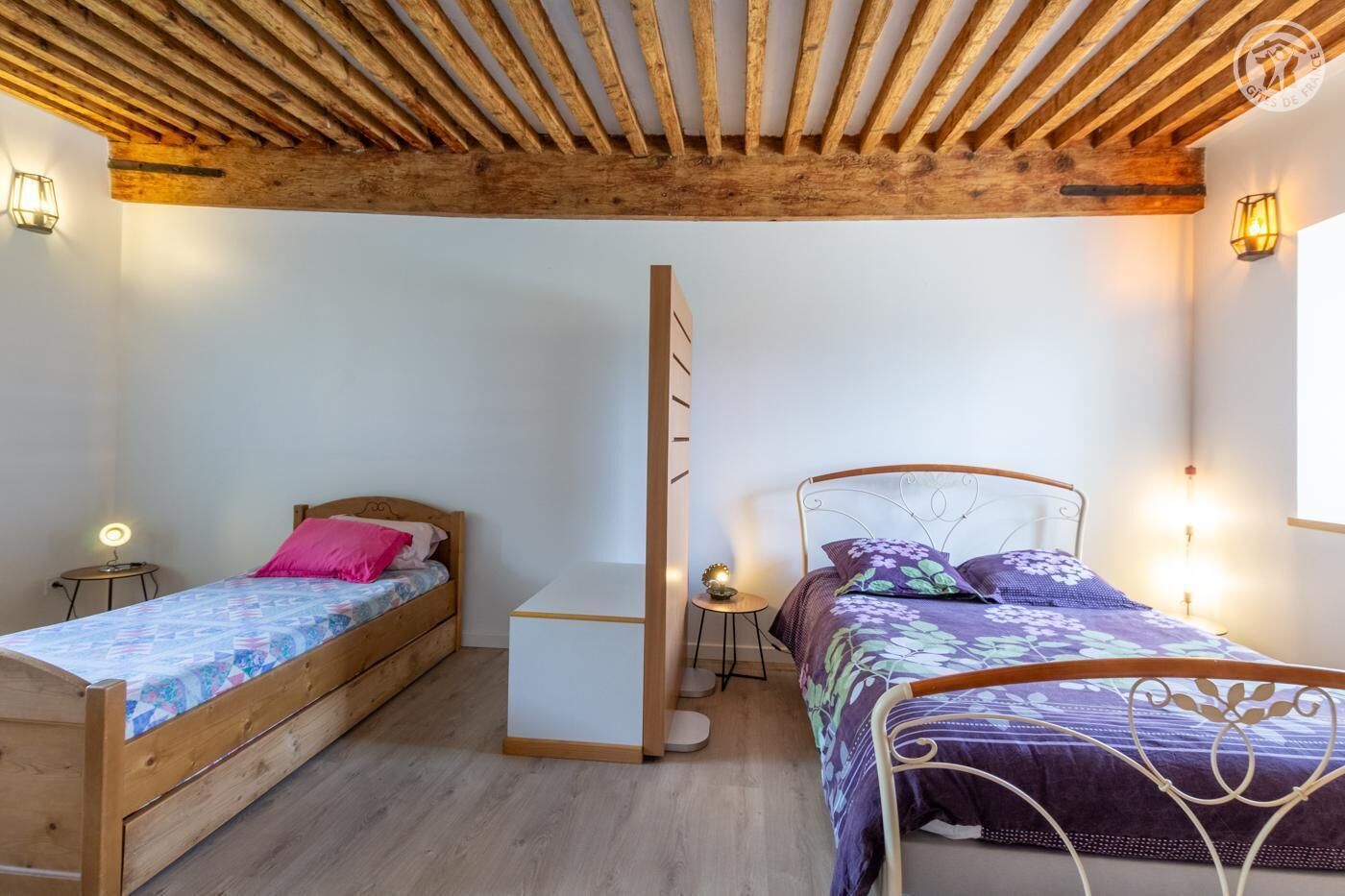 A bedroom with two wooden beds, a small white cabinet, and a wooden ceiling.