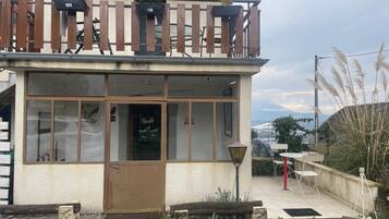 Ein zweistöckiges Gebäude mit Balkon, einer Tür und einer kleinen Außenbereich-Sitzgelegenheit.