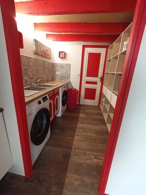 Una lavanderia con lavatrice, lavandino e un cesto rosso.