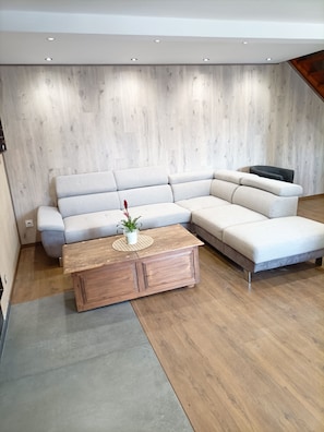 Ein modernes Wohnzimmer mit einem Ecksofa, einem Holztisch und einer Topfpflanze.
