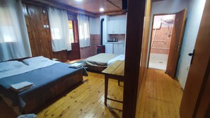 A room with two beds, a wooden floor, a kitchen area with cabinets, and a door leading to another room. - Cozy1-bedroom apartment in enjoyable view of the Tara Bridge with WiFi,fireplace (Zabljak)
