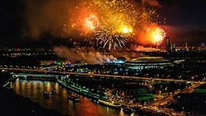 Een nachtelijk stadsbeeld met vuurwerk op de achtergrond en een rivier vol boten.
