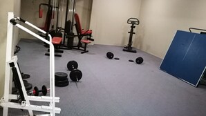 Een sportschool met gewichthefapparatuur, banken en een blauwe mat.