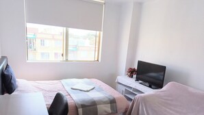 Een slaapkamer met een bed, een bureau, een televisie en een raam.