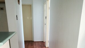 Een smalle gang met houten vloer en witte wanden.