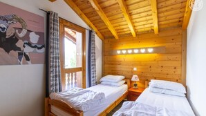 Una habitación con dos camas de madera, techo de madera y ventana con cortinas.