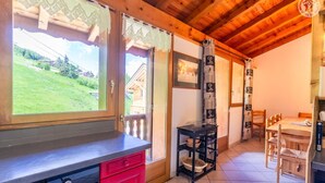 Una cocina con techo de madera, un comedor con mesa y sillas, y vistas a un paisaje verde a través de las ventanas.