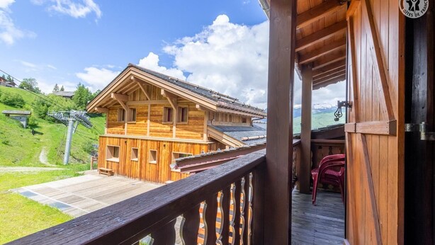 Un chalet de madera con balcón que da a un paisaje verde y un telesilla al fondo.