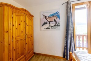 A bedroom with a wooden wardrobe, a bed, a window with curtains, and a painting of a mountain scene. - PETIT REFUGE - LA PLAGNE TARENTAISE (LA PLAGNE TARENTAISE)