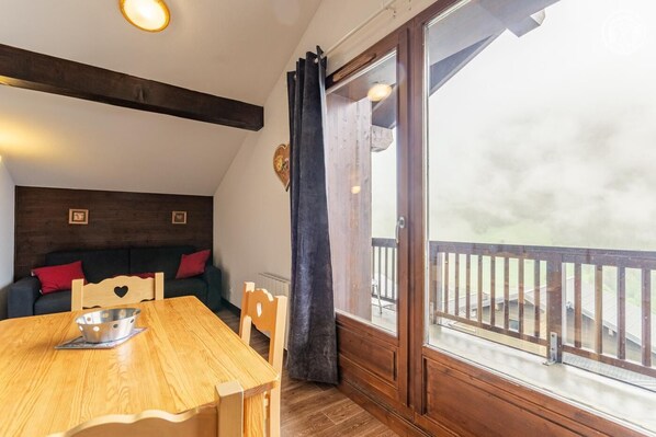 A cozy room with a wooden table, chairs, a sofa, and a large window with a view of a balcony.