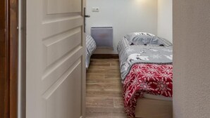 En smal gang, der fører til et soveværelse med ovenlys, en seng med mønstret sengetøj og et lille natbord.