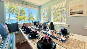 A dining area with a view of the sea, a sofa, and a table set with plates, glasses, and cutlery. - ⭐NEW⭐ Stunning Beachfront Living w/ Gameroom & Firepit Near Acadia  (Gouldsboro)