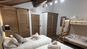 Una habitación con dos camas, armarios de madera, una escalera y una lámpara fijada a la pared.