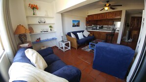 Ein Wohnzimmer mit einer Couch, einem Couchtisch und einem Essbereich, im Hintergrund eine Küche.