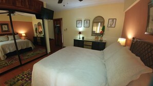 Ein Hotelzimmer mit einem großen Bett, einem Schminktisch, einem Spiegel und einem Deckenventilator.