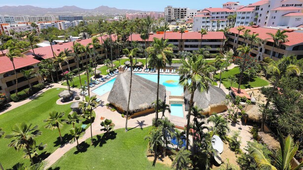 Ein Resort mit mehreren Gebäuden, einem zentralen Poolbereich und umliegenden Palmen.