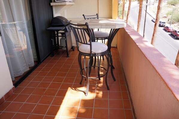 A balcony with a table and chairs, a grill, and a view of a road.